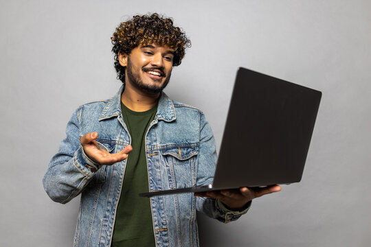 Young Indian man hold use work on laptop talk by video call waving hand say hello isolated on plain grey background . People portrait