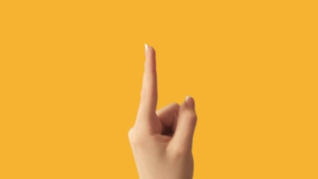 Finger pointing up. Attention gesture. Female hand showing recommending something above on orange empty space advertising background.