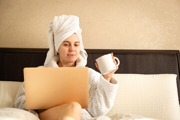 woman working at home on laptop in morning after shower holding cup of coffee