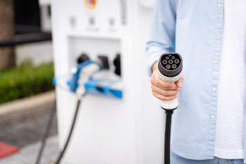 Unrecognizable Asian man holding AC type 2 EV charging connector at EV charging station.