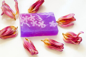 Fragrant handmade rectangular soap framed by dry tulip  lilac petals on a white background. Top view 