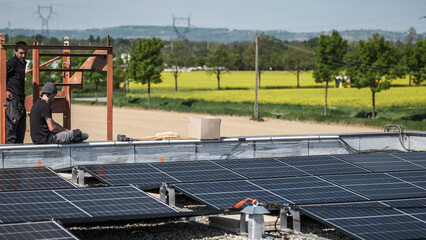 Male team engineers installing stand-alone solar photovoltaic panel system. Electricians mounting blue solar module on roof of company roof. Alternative energy concept
