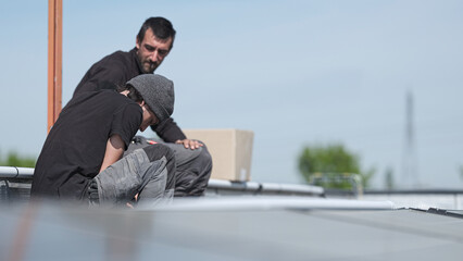 Male team engineers installing stand-alone solar photovoltaic panel system. Electricians mounting blue solar module on roof of company roof. Alternative energy concept