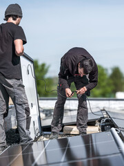Male team engineers installing stand-alone solar photovoltaic panel system. Electricians mounting blue solar module on roof of company roof. Alternative energy concept