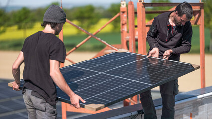 Male team engineers installing stand-alone solar photovoltaic panel system. Electricians mounting blue solar module on roof of company roof. Alternative energy concept