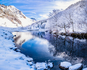 Picturesque landscape of a snowy winter mountain lake. Small lake next to the Saut Deth Pish waterfall during autumn and a snowy day, located in the Aran Valley, Pyrenees, Catalonia, Spain.