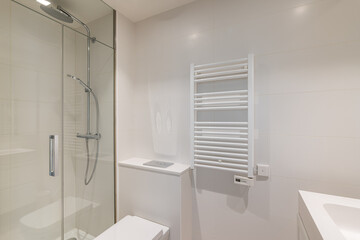 Bathroom in light colors with glossy ceramic tile walls and bright lighting. The bathroom has a shower with a glass railing and radiator for drying towels.
