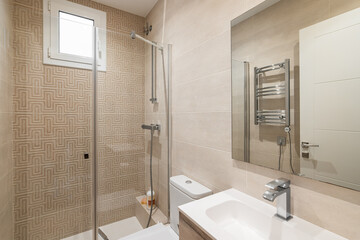 Bright bathroom in beige colors with glossy ceramic tile walls and lighting. The bathroom has a shower with a glass railing, a large mirror with a sink, a radiator for drying towels.