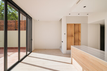 Large bright spacious kitchen with wooden furniture and closed black metal sliding glass doors with access to the terrasse. Modern design of the entrance and exit of the building.