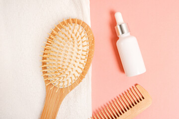 Essential oil for hair care with wooden hair comb and white towel on pink background