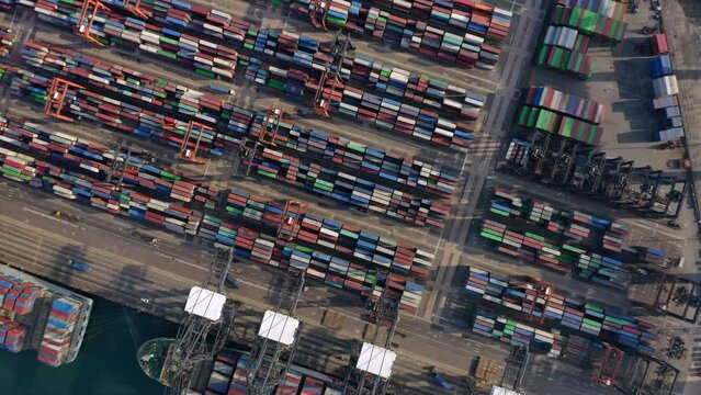 Multiple stack cranes moving over the container yard while trucks drive towards the deep sea cranes. Top down rotating drone shot