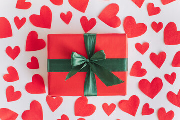 Top view of gift wrapped in red paper on white background with red paper hearts. Flat lay, Valentine's Day background love concept.
