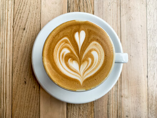 A cup of coffee latte on a wooden table. A mug of flat white coffee, latte, cappuccino on a wooden background. Coffee art. Heart flower shape latte art
