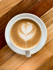 A cup of coffee latte on a wooden table. A mug of flat white coffee, latte, cappuccino on a wooden background. Coffee art. Heart flower shape latte art