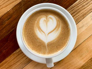 A cup of coffee latte on a wooden table. A mug of flat white coffee, latte, cappuccino on a wooden background. Coffee art. Heart flower shape latte art