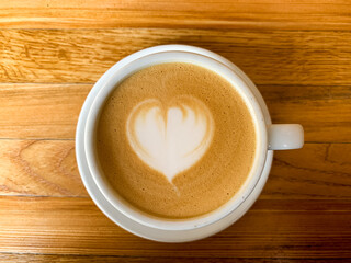 A cup of coffee latte on a wooden table. A mug of flat white coffee, latte, cappuccino on a wooden background. Coffee art. Heart flower shape latte art