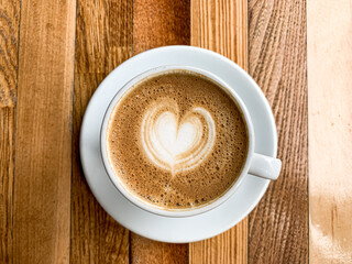 A cup of coffee latte on a wooden table. A mug of flat white coffee, latte, cappuccino on a wooden background. Coffee art. Heart flower shape latte art
