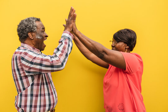 Senior Man And Woman Giving High-five To Each Other Against Yellow Background