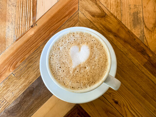 A cup of coffee latte on a wooden table. A mug of flat white coffee, latte, cappuccino on a wooden background. Coffee art. Heart flower shape latte art