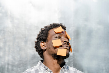 Contemplative man with yellow adhesive notes on face in front of wall