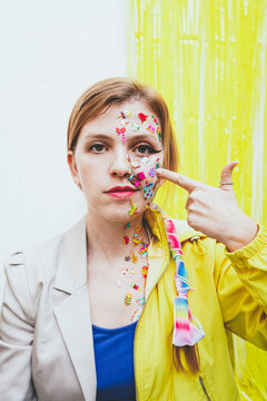 Woman pointing at stickers on face in front of two tone wall