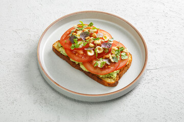 Toast with guacamole and slices of fresh tomatoes with fried hazelnuts on top. Vegetarian cuisine