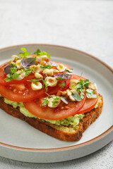 Toast with guacamole and slices of fresh tomatoes with fried hazelnuts on top. Vegetarian cuisine