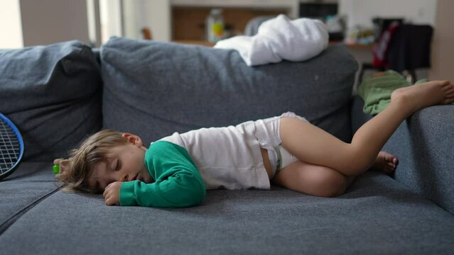 Funny little boy laying on sofa sleeping during afternoon nap. Baby toddler wearing diapers asleep on couch