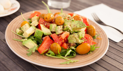 dish of fresh vegetables arugula, avocado, cherry tomatoes with olives on dining table