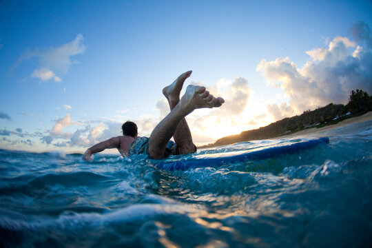 A young man's feet dominate the image as he  paddles past at  Monster Mush, on the north shore of Oahu, Hawaii