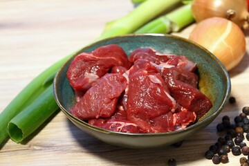 Raw deer meat for venison ragout or goulash. Bowl with pieces of deer meat on cutting board, fresh vegetable and spices for cooking around.