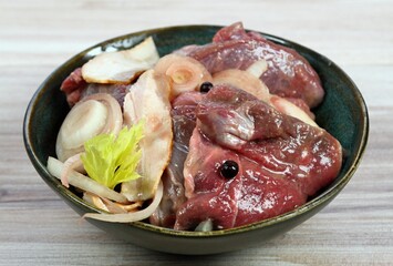 Fresh deer meat  marinated in red wine with bakon, onion, garlic and juniper berries. Bowl with pieces of deer meat on  wooden table.