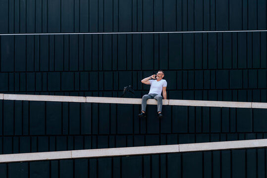 Portrait of mature bearded man on the phone sitting on a wall outdoors