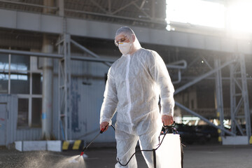 Fototapeta na wymiar Man dressed white protective overalls spraying surface antibacterial sanitizer sprayer during quarantine