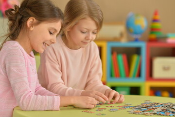Fototapeta premium little girls collecting puzzle pieces while sitting at table