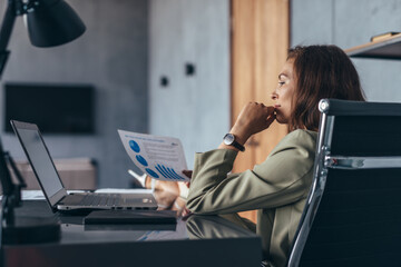 Woman studying data on paper sitting at her desk in the office