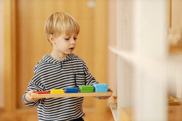 A boy at kindergarten is holding a colorful wooden educational toy and preparing to play with it.