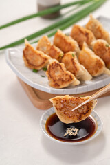 Pan-fried gyoza dumpling jiaozi in a plate with soy sauce on white table background.