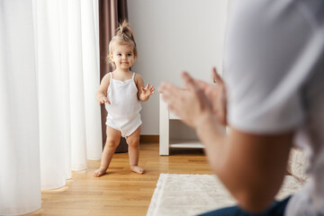 A baby girl is standing on her own and learning how to walk.