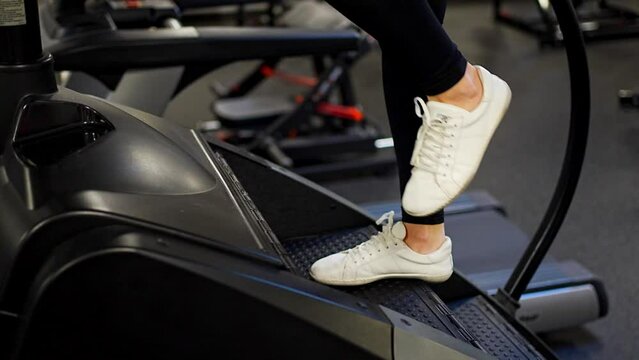 Woman walking on climbing machine in a fitness club, gym, cardio workout. Close up on feet.