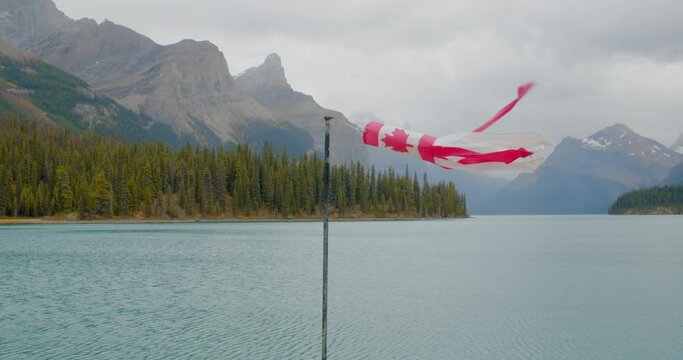Canadian flag waking with the wind near a stunning green water lake surrounded by tall mountains in the Canadian rockies.