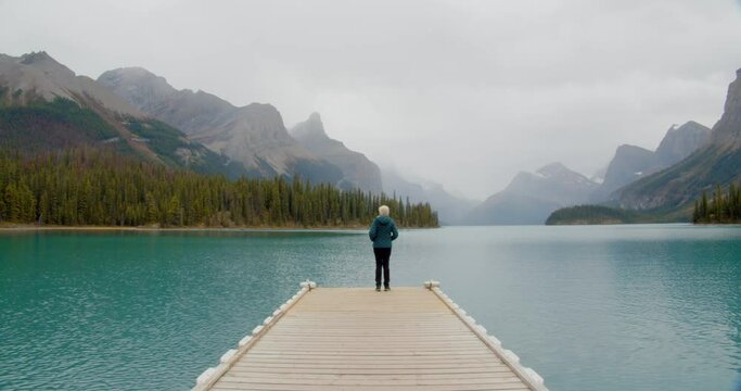Outdoorsy woman looking mountain the horizon on the edge of a small pier floating on a stunning green water glacial lake nestled in the Canadian rocky mountains