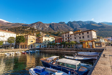 Fototapeta na wymiar Small port of Malcesine village with small boats moored. Famous tourist resort on the coast of Lake Garda (Lago di Garda). Verona province, Veneto, Italy, Europe. Mountain range of Monte Baldo.
