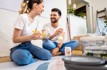 Young couple sitting on the floor choosing color for painting the wall in their home.