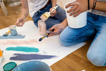 Young couple sitting on the floor choosing color for painting the wall in their home.