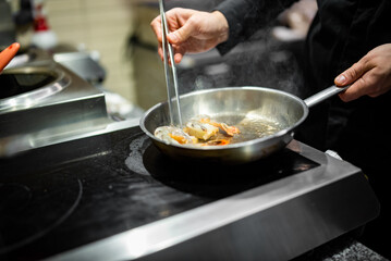 man chef cooking fried shrimp in frying pan on kitchen