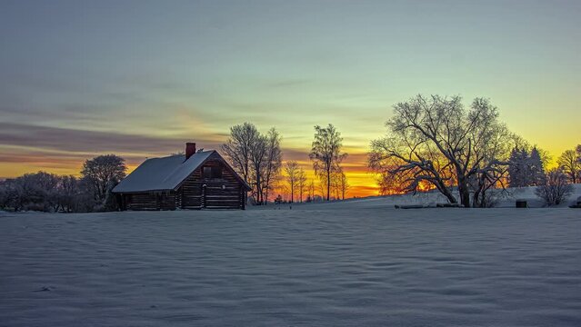 Stunningly colorful sunrise beyond a cabin on a winter landscape - time lase