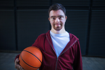 Portrait of young man with down syndrom holding basketball ball.