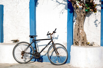 Fototapeta na wymiar bicycle on the street in Greece style with white wall and blue frames and old tree 