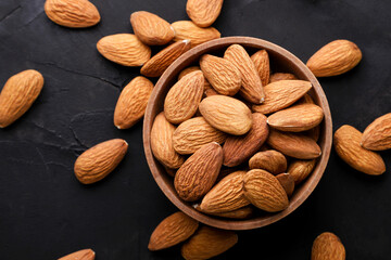 Almond nuts in a wooden plate on a dark background. Top view